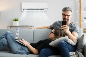 Couple Sitting On Sofa With Ductless Unit On Wall Behind Them